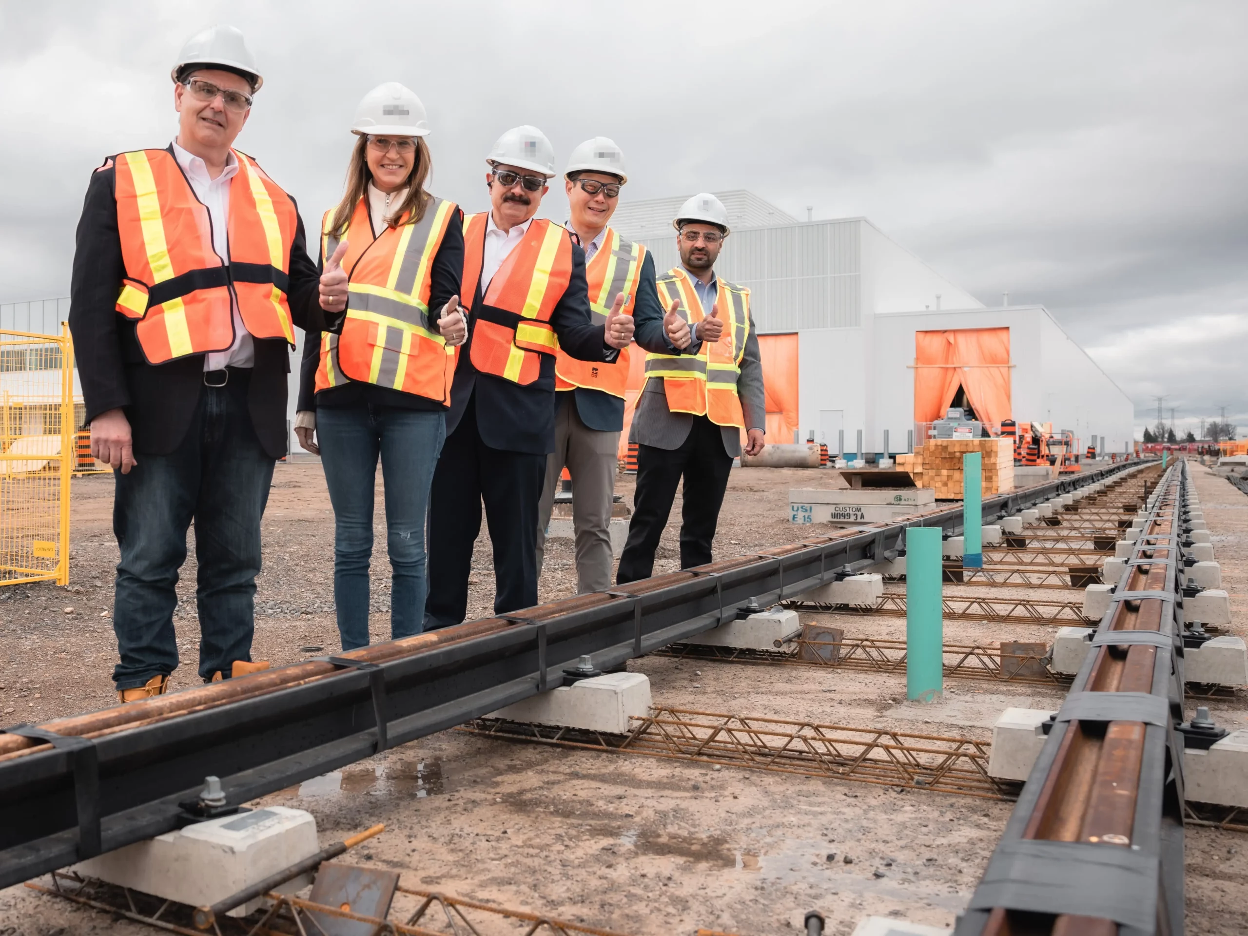 MPP Sabawy, Minister Mulroney, Minister Cho, and other MPPs wearing protective construction gear give a thumbs up in front of a section of track for the Hazel McCallion LRT.