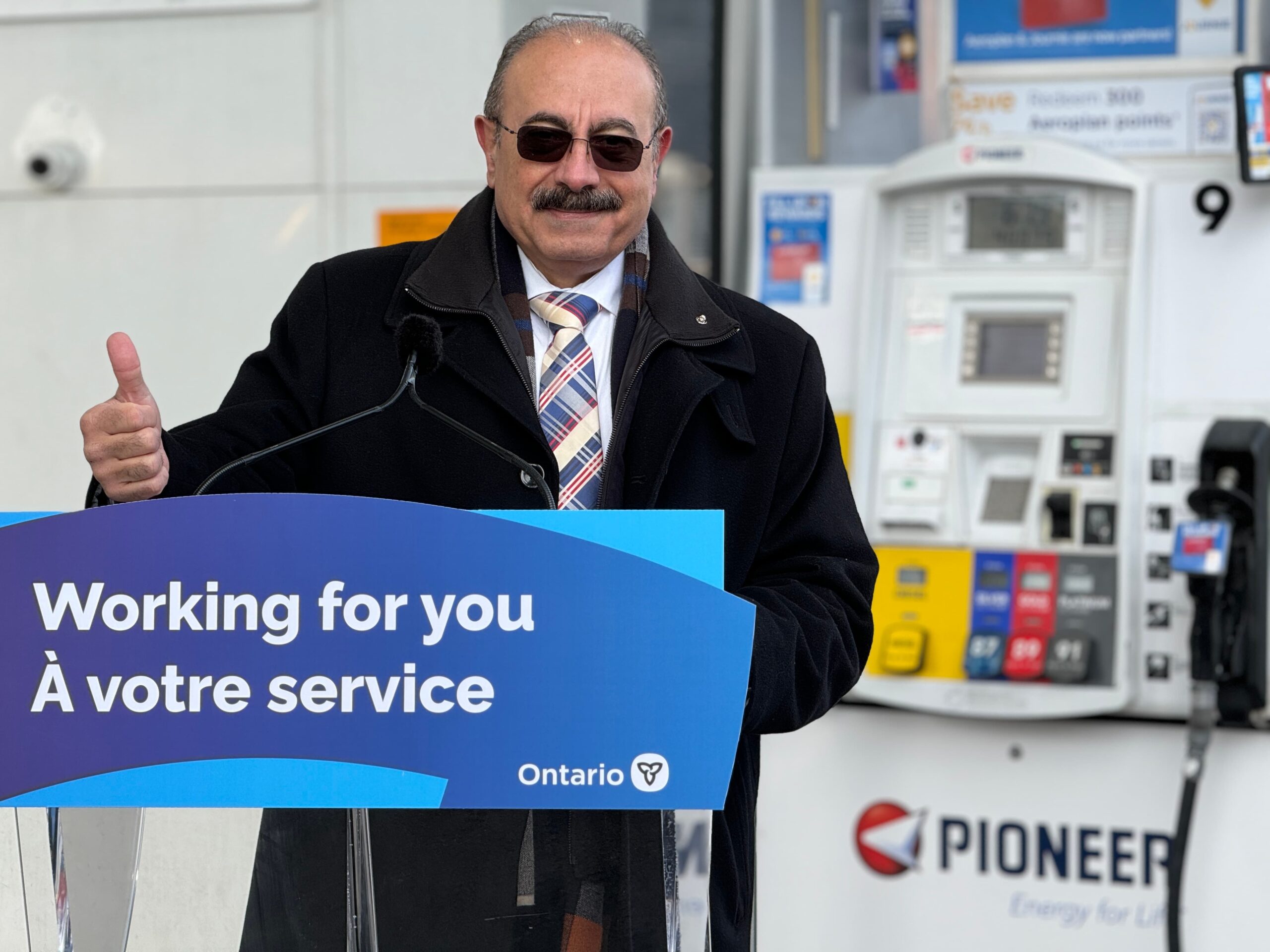 MPP Sabawy gives a thumbs up in front of a gas station pump and a sign that reads "Working for you"